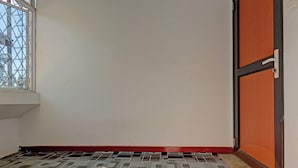 A room with a patterned floor, a window with a metal grid, and a wooden door with a black frame.