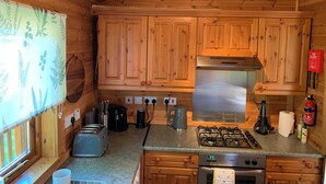 A wooden cabin kitchen with a gas stove, oven, and a coffee maker. - Lodge With River View - Sleeps 6 - pet Friendly (Hawick)