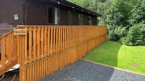 A wooden cabin with a nameplate reading "The Bridge," a gravel path leading to the entrance, and a lush green landscape in the background. - Lodge With River View - Sleeps 6 - pet Friendly (Hawick)