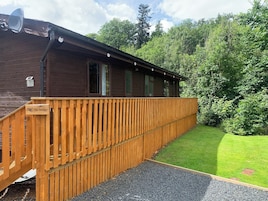 A wooden cabin with a nameplate reading "The Bridge," a gravel path leading to the entrance, and a lush green landscape in the background.