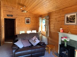 Un interior de cabaña acogedor, con un sofá de cuero, una chimenea y paredes de madera.