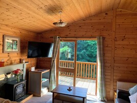 A cozy cabin interior with a wooden ceiling, a television mounted on the wall, a small table, and a window with curtains.