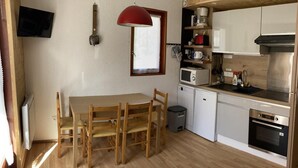 Une cuisine compacte comprenant une table à manger, des chaises en bois, un luminaire suspendu rouge, un four à micro-ondes, une cuisinière et une petite poubelle.