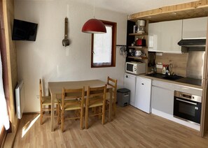 A compact kitchen with a dining table, wooden chairs, a red pendant light, a microwave, a stove, and a small trash bin. - 230m from resort center, 1st floor, balcony, parking, tv, ski locker, 23m², Valloire (Valloire)