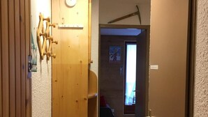 Un couloir étroit aux murs en bois, avec une porte en bois sur la droite. Sur la gauche, on aperçoit une étagère en bois ornée d’une étoile de David.