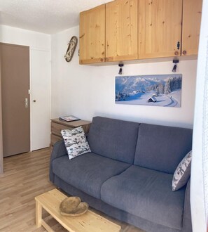 A living room with a grey sofa, wooden cabinets, a small table, and a painting of a snowy landscape.