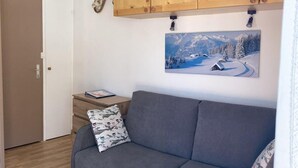 Un salon avec un canapé gris, des meubles en bois, une petite table et un tableau représentant un paysage enneigé.