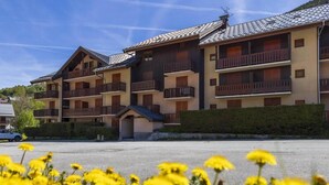 Un hôtel à plusieurs étages, doté de balcons, d’un parking et agrémenté de fleurs jaunes au premier plan.