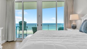 Une chambre avec un grand lit, une vue sur l’océan et un balcon équipé de chaises.