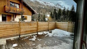 A wooden deck with snow on the ground, a wooden fence, and a mountain in the background.