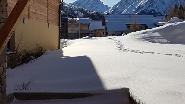 A wooden staircase leading to a building with a view of snow-covered mountains and a lake.