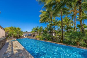 A swimming pool with clear blue water, surrounded by palm trees and a stone deck.