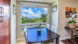 A dining area with a large window offering a view of a residential neighborhood and a tropical landscape.