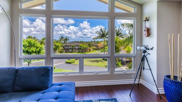 A room with a large window offering a view of a residential area, a telescope on a tripod, and a blue sofa.