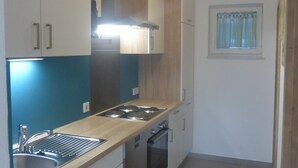 Una cocina compacta con armarios blancos, un lavamanos de acero inoxidable, una estufa y una ventana con cortinas.