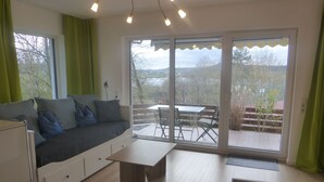 A modern room with a sofa, a dining table, and a large sliding glass door leading to an outdoor patio. - Ferienwohnung Lehrberg - Moderne Wohnung mit Wallbox für E-auto (Lehrberg)