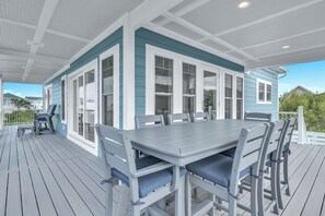A covered outdoor deck with a dining table and chairs, surrounded by a white railing.