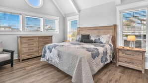 A bedroom with a large bed, wooden nightstands, a wooden dresser, and a skylight. - Fanta Sea: Modern Home Built in 2023 with Private Pool, Elevator (Oak Island)