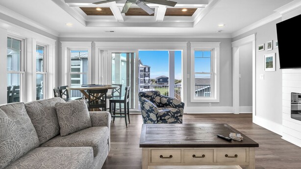 A spacious living room with a ceiling fan, a sofa, a coffee table, and a view through large windows. - Fanta Sea: Modern Home Built in 2023 with Private Pool, Elevator (Oak Island)