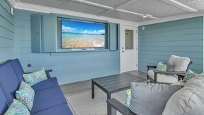 A room with a large window overlooking a beach, a sofa, a table, and a chair. - Fanta Sea: Modern Home Built in 2023 with Private Pool, Elevator (Oak Island)
