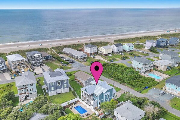 An aerial view of a coastal residential area with houses, a beach, and a swimming pool.