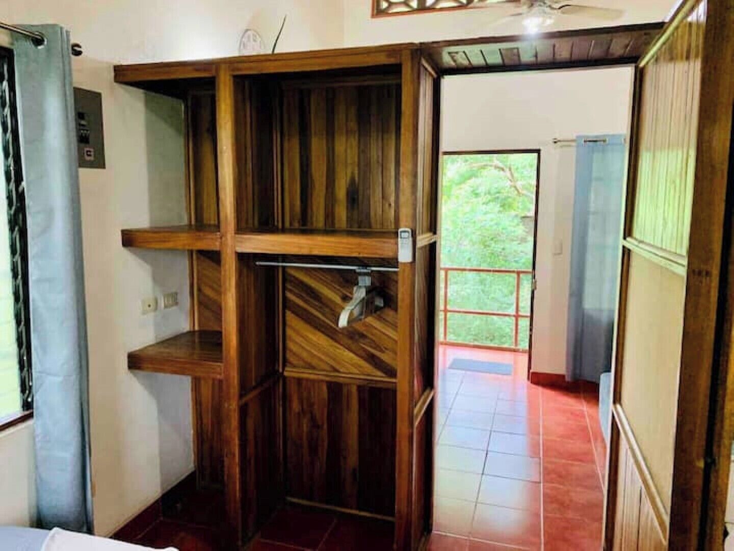 A room with a wooden shelving unit, a tiled floor, and a view of greenery outside.