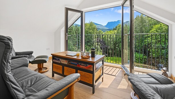 En moderne stue med et stort glasdør, der fører ud til en balkon med udsigt til et bjerglandskab.