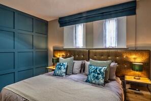 Relax in this serene bedroom with a large bed, pillows, and a textured blanket, surrounded by a dark paneled wall and a tufted headboard.