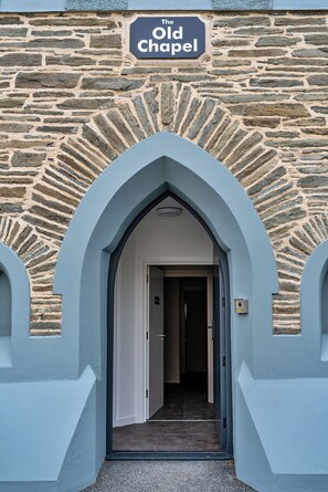 Enter The Old Chapel through a light blue archway, leading to a historic stone building with a unique pattern.