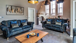 Een ruime woonkamer met twee blauwe banken, een houten salontafel en een groot abstract schilderij aan de muur.