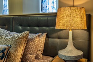 Relax in a stylish bedroom with a dark leather headboard, modern lamp, and patterned pillows.