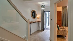 A hallway with a wooden console table, a mirror, and a patterned armchair. - Lobster House (Newquay)
