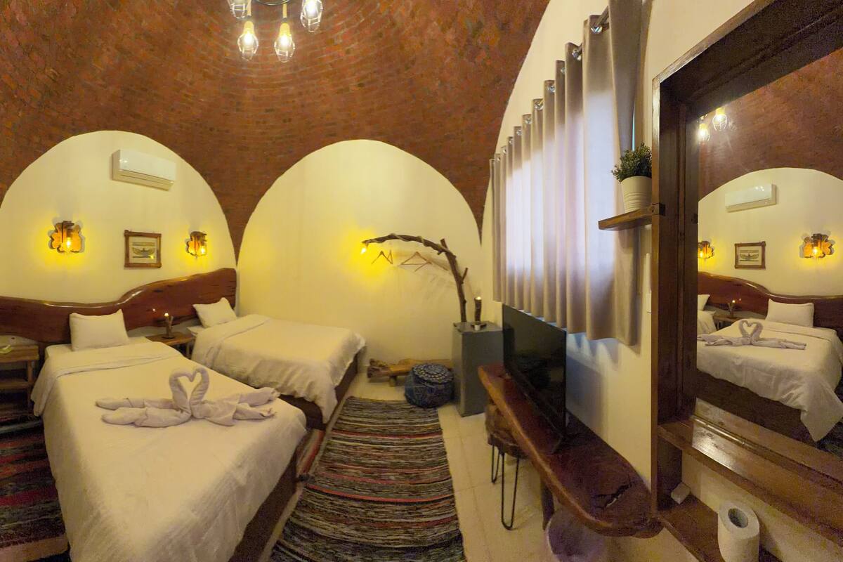 A hotel room with two beds, a TV, a mirror, and a wooden ceiling.