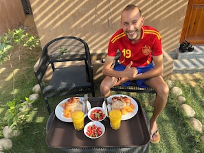 A person sitting on a chair outdoors with a tray containing food and drinks.