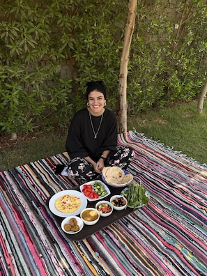 A person sitting on a colorful striped blanket outdoors with a meal laid out in front.