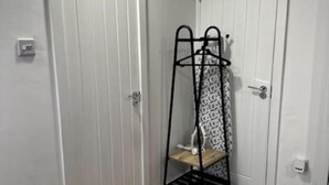 A room with a wooden floor, two white doors, and a metal coat rack with a patterned cloth. - Perfect stay with Dallas Studio (Hayes)