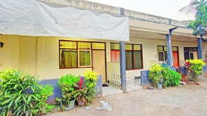 A building with a covered porch, multiple windows, and potted plants. - Hotel O Penginapan 3 Bersaudara Near Pasar Sengkol (Janapria)