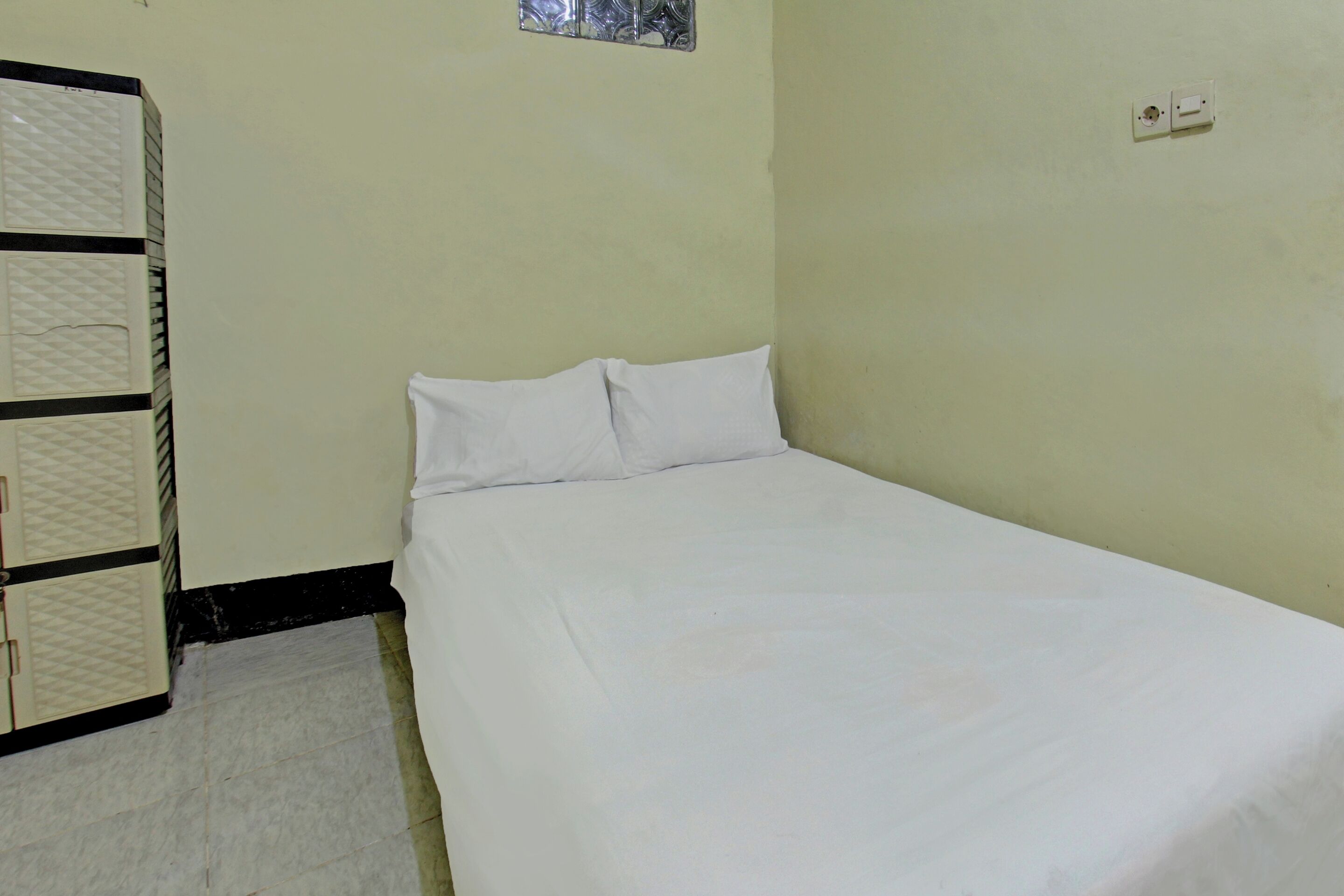 A small, single-bed room with a plain bed, a wardrobe, and a small window.