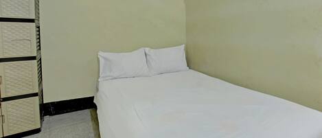 A small, single-bed room with a plain bed, a wardrobe, and a small window.