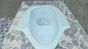 A squat toilet with a stone-patterned floor and a plain wall. - Hotel O Penginapan 3 Bersaudara Near Pasar Sengkol (Janapria)