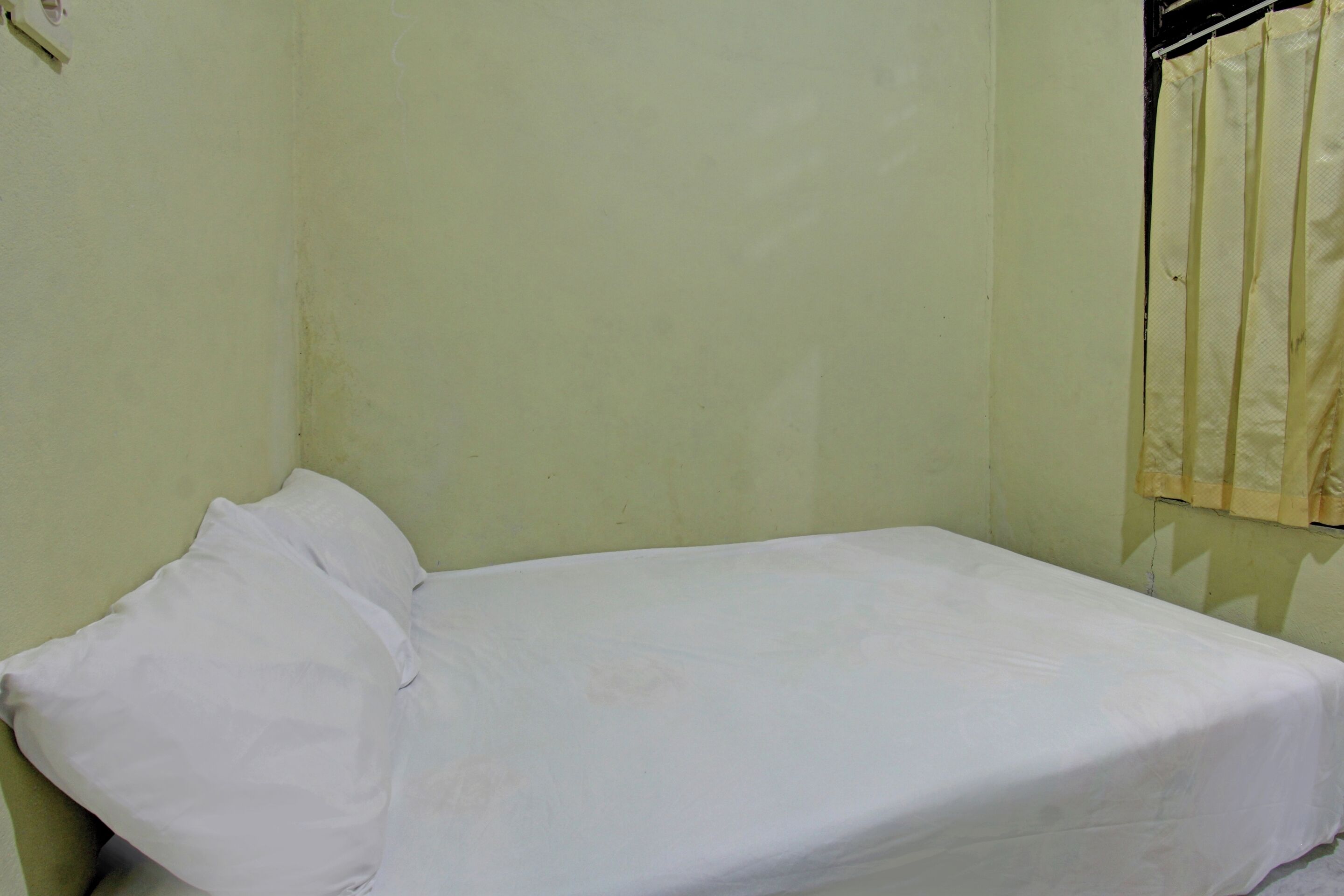 A small, single-bed room with a plain bed and a window with a curtain.