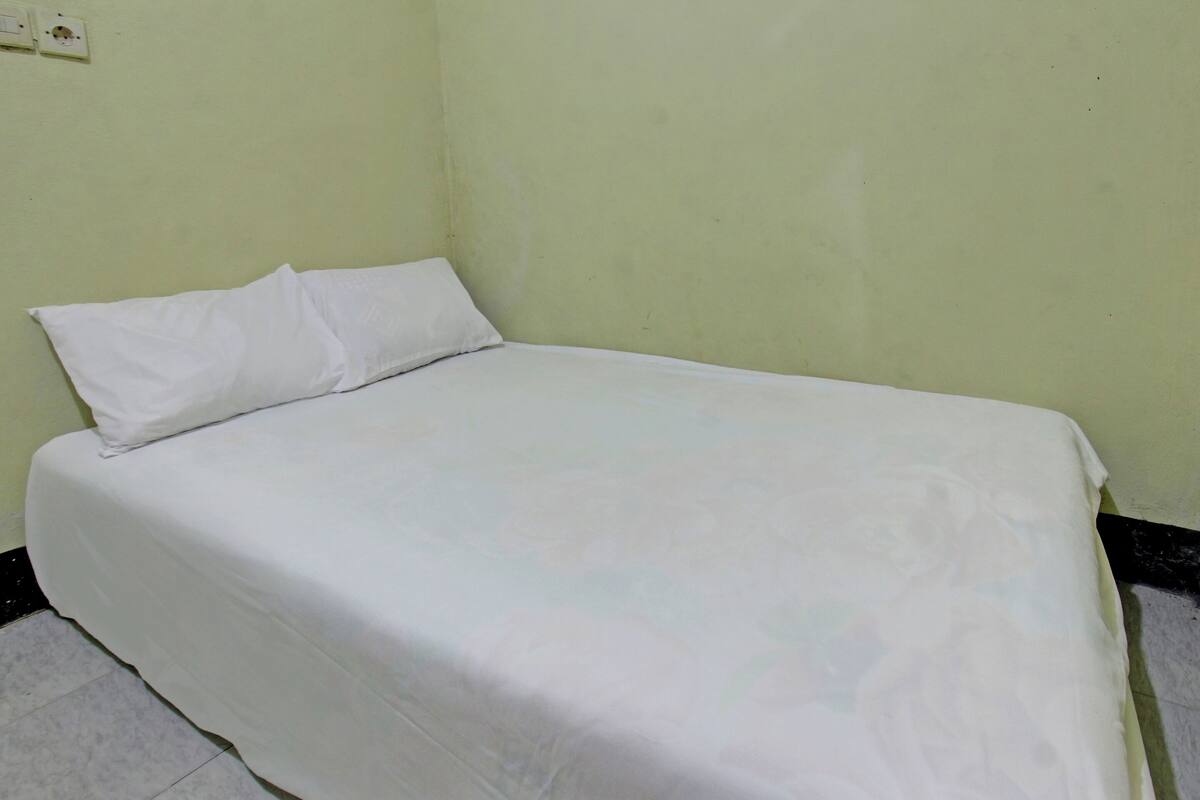 Ein Zimmer mit einem Einzelbett, einer schlichten weißen Bettdecke und einem weißen Kopfkissen.