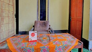 A room with a table covered by a colorful tablecloth, a chair, and a sign on the table. - Hotel O Penginapan 3 Bersaudara Near Pasar Sengkol (Janapria)