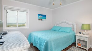 A bedroom with a bed, a desk, a lamp, and a painting. - Southwinds G16 (Ocean View) (Atlantic Beach)