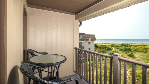 A balcony with a table and chairs, overlooking a beach and buildings. - Southwinds G16 (Ocean View) (Atlantic Beach)