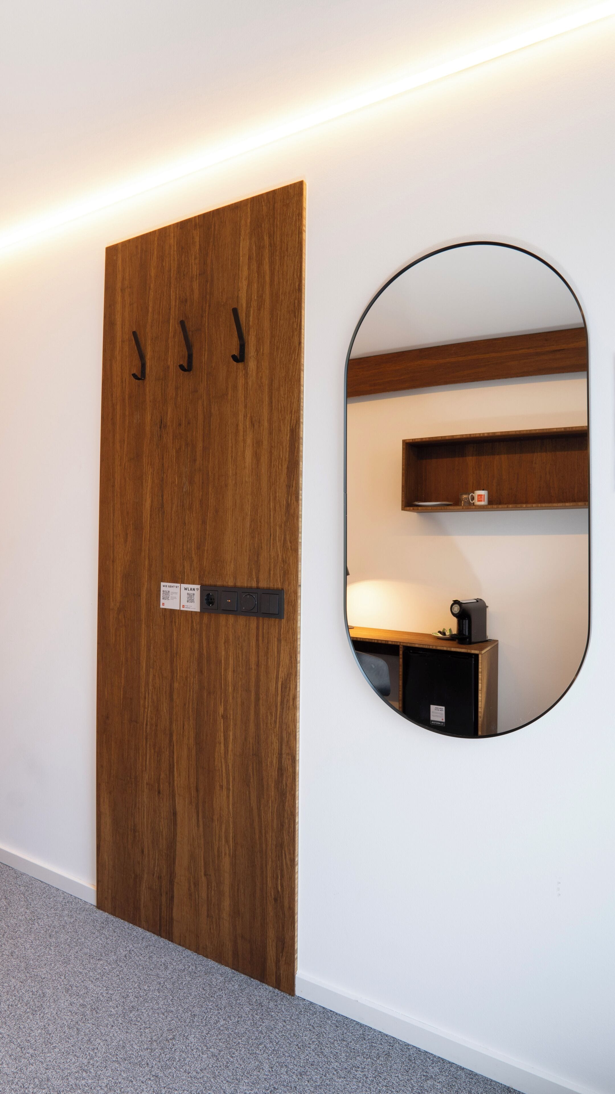 A wooden door with a label and hooks, a round mirror, and a small shelf with a coffee maker.