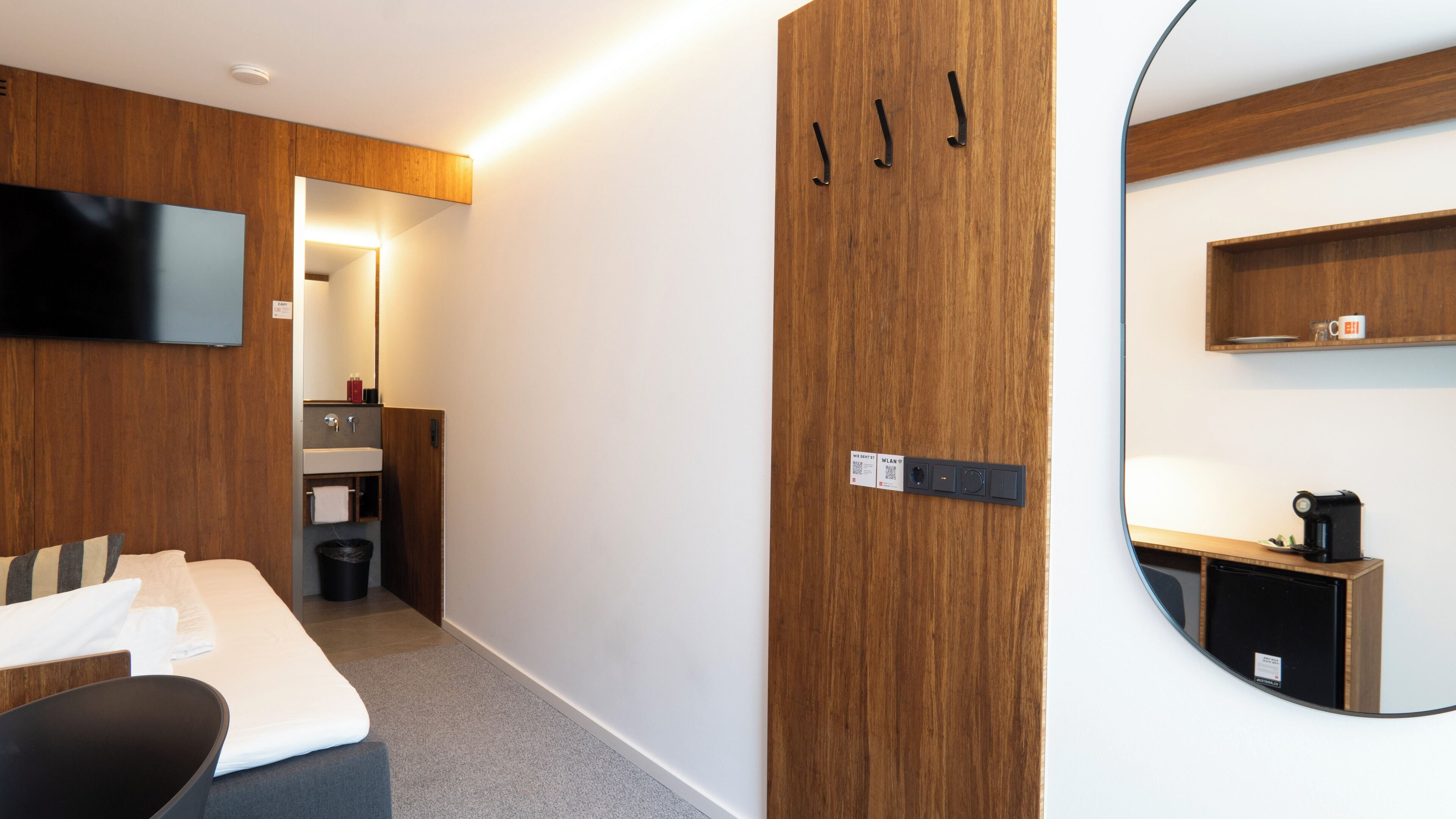 A hotel room with a bed, a TV, a mirror, a small kitchenette, and a wooden wardrobe.
