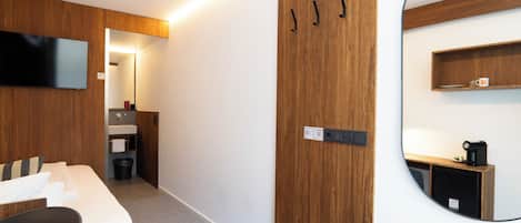 A hotel room with a bed, a TV, a mirror, a small kitchenette, and a wooden wardrobe.