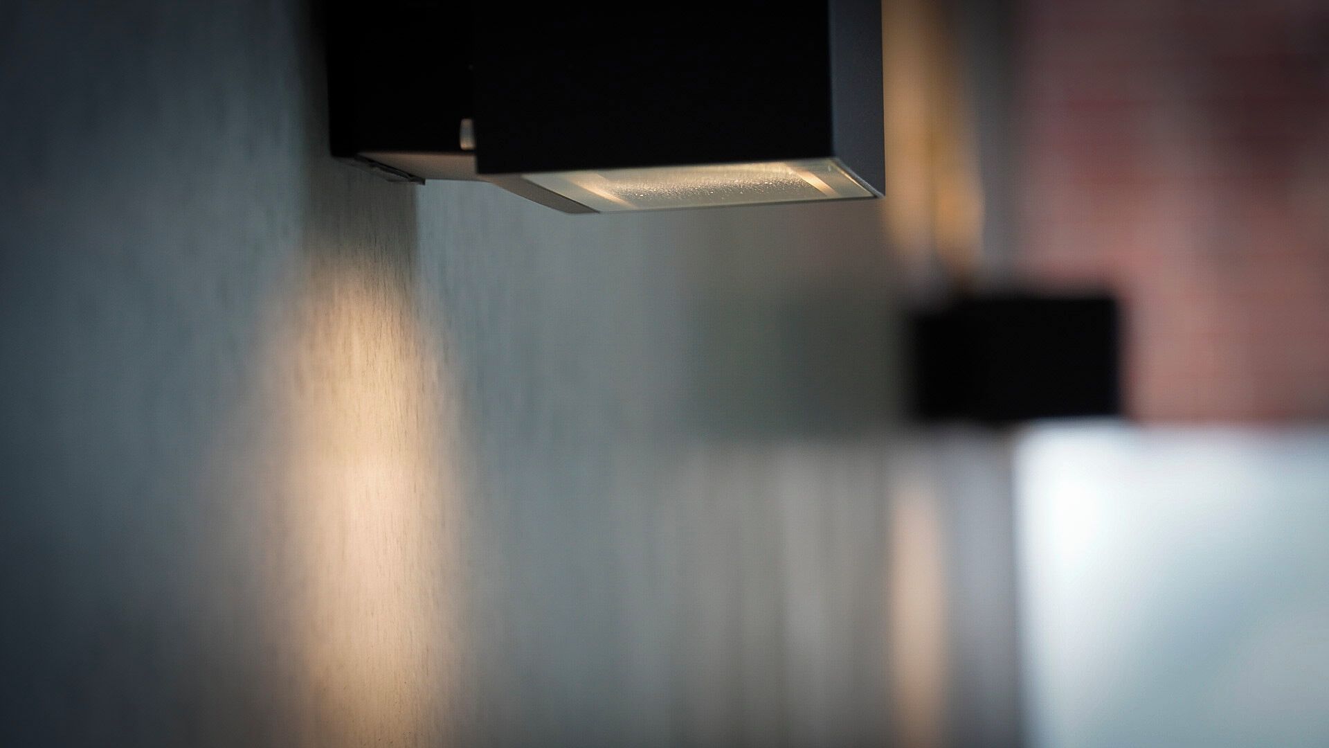 A close-up of a modern, minimalist light fixture with a metallic finish, casting a soft glow.
