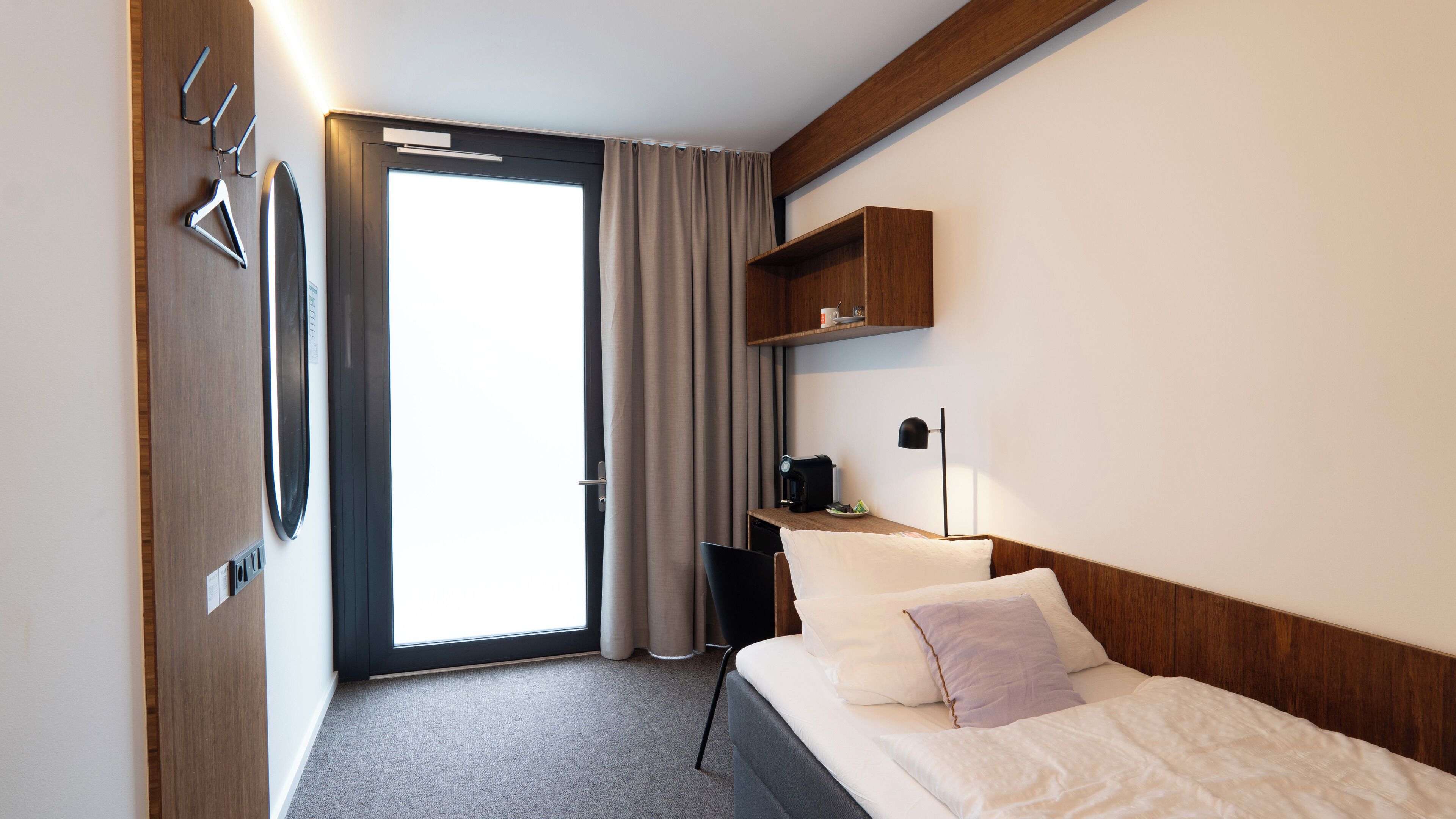 Una habitación de hotel con cama, escritorio con lámpara, cafetera y armario.